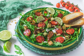 Bowl of fresh vegetable salad: arugula, fresh and dried cherry tomatoes, pine nuts and cheese on a white wooden background