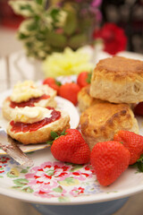  Scones  on a floral plate with jam and cream with fresh strawberries. Flowers in the background