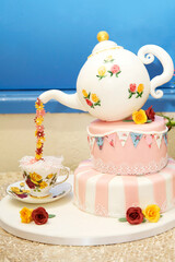 Pink and white celebration cake with teapot pouring sugar flowers into cup