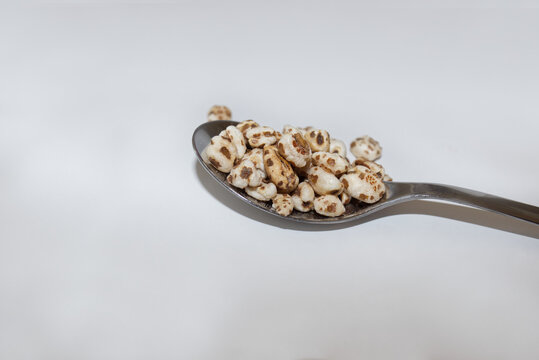 A tablespoon of puffed wheat on a white background 