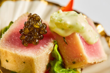 Close up of rare seared Ahi tuna slices with fresh vegetable salad on a plate. Shallow dof