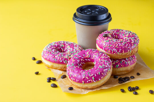 Takeaway coffee cup with coffee beans and pink glaze donuts with colorful sprinkles, pink background.