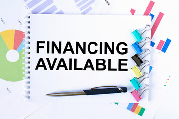 Notepad with text Financing Available, paper clips, blue pen on financial diagrams