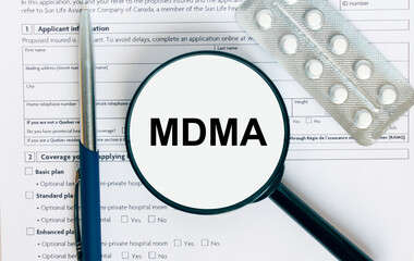 Magnifying glass with text MDMA inside lies on medical documents with pills and a blue metal pen