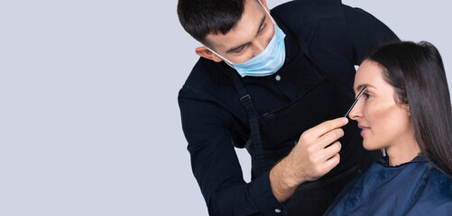 Banner,long format. Cropped photo of male makeup artist in medical mask and brunette model girl. Work and beauty during a pandemic.