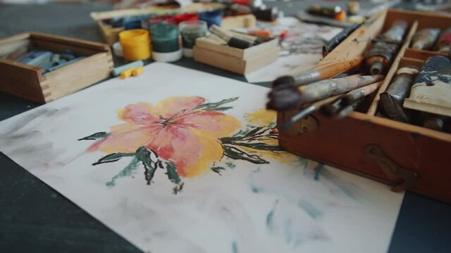 Close up shot of professional art supplies and picture of beautiful flower on worktable of artist