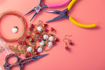 Tools and materials for hobbies. Creating handmade jewelry. Pendants, wire, pliers, etc. on a pink background. Working space for creative workshops at home