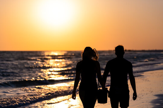 Sunset sun in Siesta Key, Florida at Sarasota, USA with coast ocean gulf of mexico, young couple silhouette walking on beach, holding hands