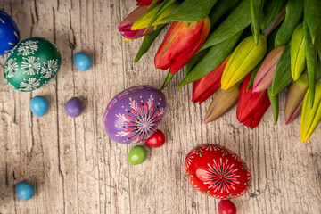 Painted Eggs In Basket With Tulips On Natural Wooden Plank