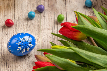 Painted Eggs In Basket With Tulips On Natural Wooden Plank