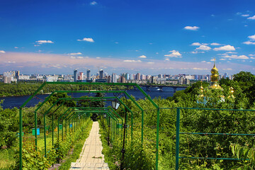 Path to a garden with beehives on the site of the Kyiv Pechersk Lavra, beautiful view of the Dnieper river and a residential area with high-rise buildings, Kyiv, Ukraine