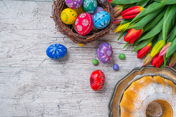 Painted Eggs In Basket With Tulips On Natural Wooden Plank