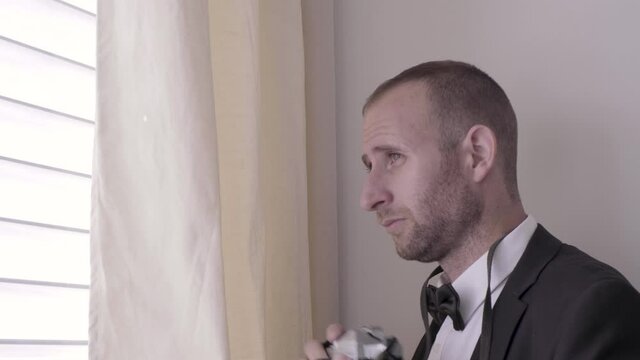 man in tuxedo taking a pictures and hiding behind a window. undercover detective spying with a camera and photographing. photographer stalking and paparazziing people outside through the window.