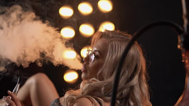 Sexy girl smoking a hookah emits clouds of smoke