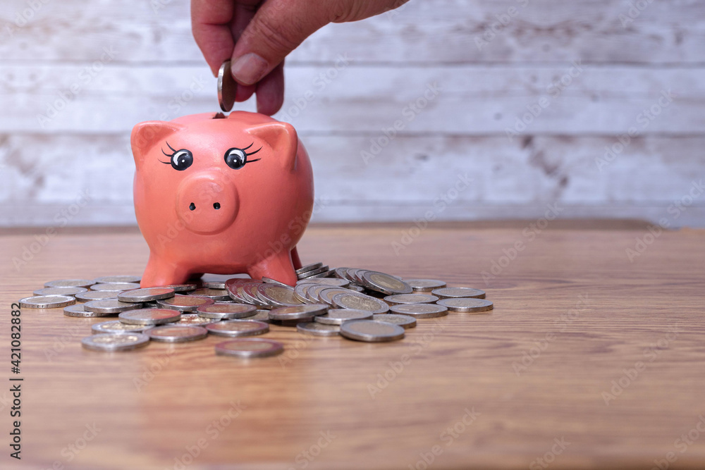 Wall mural hand inserting a money coin into the piggy for saving money wealth in concept of economy