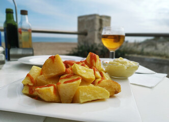 Aperitivo de patatas bravas y cerveza frente al mar