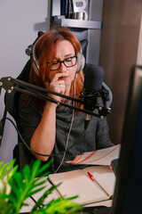 Mujer caucásica de mediana edad grabando un podcast desde casa en el escritorio junto a un...