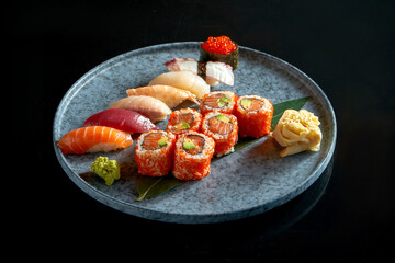 Californian sushi roll set with salmon in tobiko caviar and various sushi. Sushi with salmon, tuna, shrimp. Japanese rolls served in a blue plate. Isolated on black background