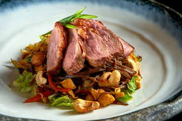 Sweet and sour buckwheat noodles with duck, peanuts, vegetables and onions, served in a white bowl. Wok noodles. Isolated over black background. Street thai food