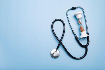 Stethoscope and hourglass on a blue background. Heart or breath check by doctor, missed elapsed time.