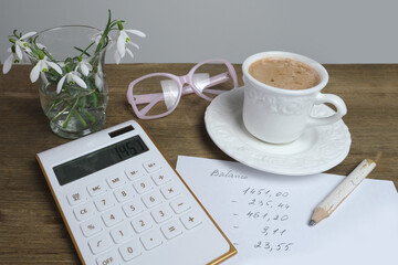 electronic white calculator, a cup of coffee, cappuccino, women's glasses, records of calculations, concept of recording debit and credit, the workplace of accountant, home economics, coffeetime