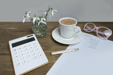 electronic white calculator, a cup of coffee, cappuccino, women's glasses, records of calculations, concept of recording debit and credit, the workplace of accountant, home economics, coffeetime