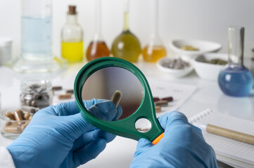 Doctor or pharmacist examining a medical capsule with a magnifying glass