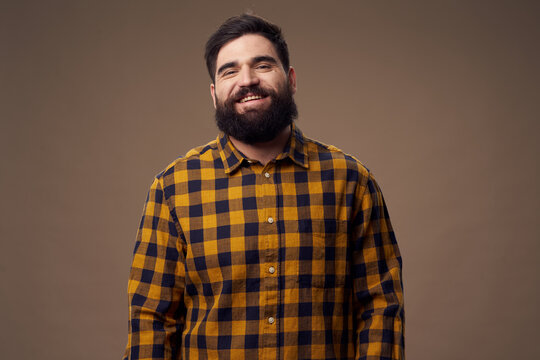 A happy man with a bushy beard is smiling at the camera and a plaid shirt