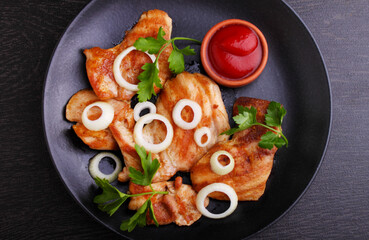 Grilled chicken fillet with tomato sauce and greens on a black background. Top view.