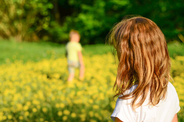Obraz premium girl in the foreground and boy in the background playing on a green field full of yellow dandelions