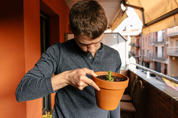 Hombre joven caucásico mirando el estado de sus plantes en la terraza de su casa durante el atardecer 