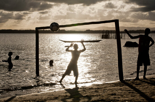Meninos jogando bola &agrave; beira-mar.