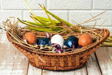Easter eggs on straw in a wicker basket on an old wooden table surface.
