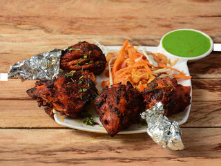 Tandoori chicken - prepared by roasting chicken marinated in yoghurt and spices in a tandoor, served over a wooden rustic background. selective focus