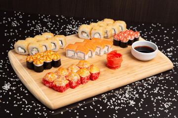 Big sushi set on light wooden dish isolated on black background