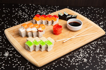 Big sushi set on light wooden dish isolated on black background