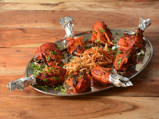 Tandoori chicken - prepared by roasting chicken marinated in yoghurt and spices in a tandoor, served over a wooden rustic background. selective focus