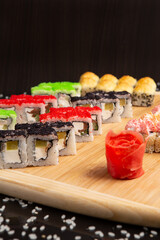 Big sushi set on light wooden dish isolated on black background