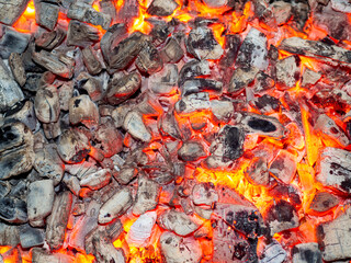 Detailed texture of burning charcoal in a campfire. Background of embers smouldering in the fireplace. Barbecue coals from firewood. Fire eco friendly organic fuel in grill top view.