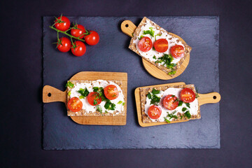 healthy crackers with cheese, cherry tomatoes with fresh herbs on a black background. Top view