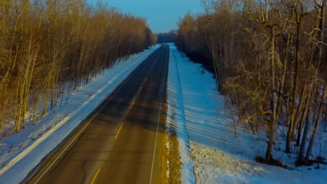aerial panout over curvy snowy winter forest sunrise glow reflection of a terrain around a highway freeway road as the sun reflects on the trees and dense coverages of a reflective shadowing path 2-2