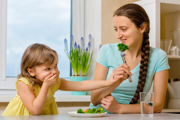 Girl doesn't want eat healthy vegetables. Kid looks with disgust at broccoly. Mother convinces her...