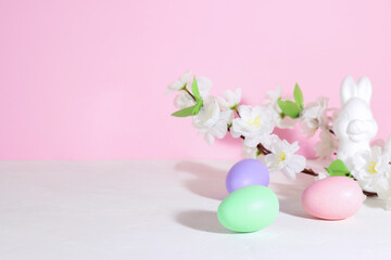 Easter eggs, pink, green and lilac, on a concrete white table, next to bunnie and flowers, on a pink background. Pastel shades.