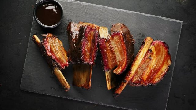 Smoked beef ribs on a black slate board, top view, rotating around its axis. Smoked beef meat with bone on a black background.