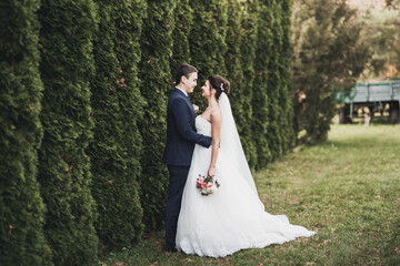 Stylish couple of happy newlyweds walking in the park on their wedding day with bouquet