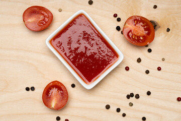 tomato sauce in white bowl and tomatoes on wooden background