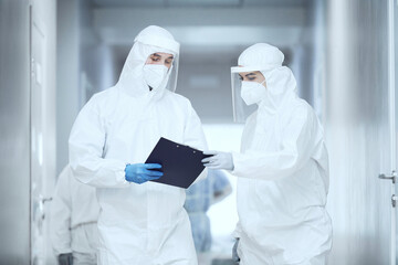 Two doctors in protective uniforms standing at the hospital corridor and examining medical card...