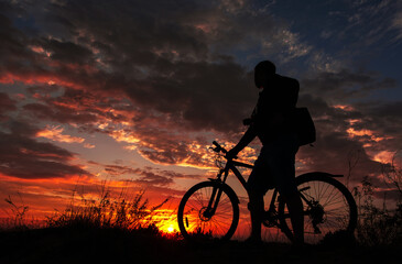 Obraz premium cyclist with a bicycle, in the background fiery sunset.