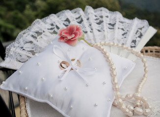Wedding arrangement on a background of a mountain landscape. Wedding rings and a red flower pearl necklace on a lace pillow.