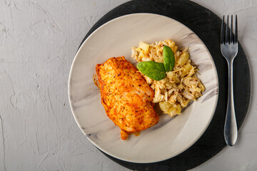 Baked chicken breast with salad on a plate decorated with spinach next to a fork on a gray background on a round black stand.